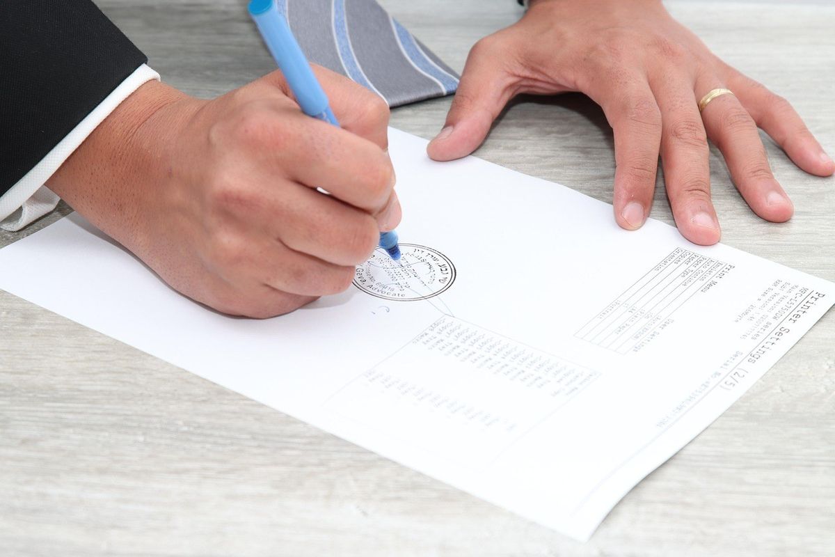 Main droite écrivant sur un document avec un stylo bleu, main gauche posée dessus, table en bois Main droite écrivant sur un document avec un stylo bleu, main gauche posée dessus, table en bois