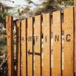 Barrière en bois avec inscription CAMPING et flèche, entourée de végétation