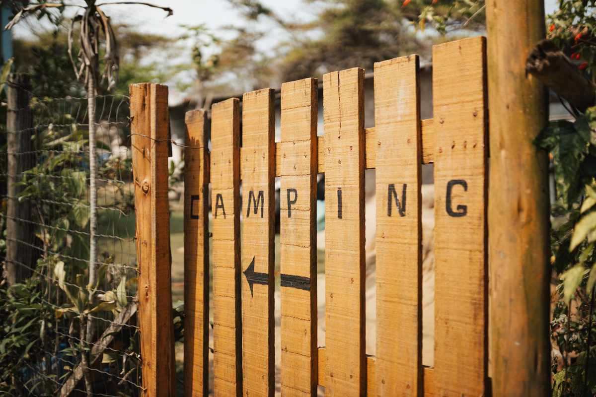 Barrière en bois avec inscription CAMPING et flèche, entourée de végétation