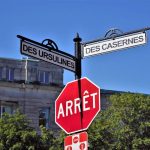 Panneau d'arrêt rouge, deux panneaux de rue, bâtiment derrière, arbres, ciel clair