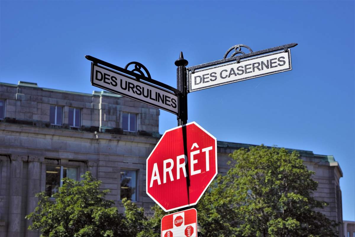 Panneau d'arrêt rouge, deux panneaux de rue, bâtiment derrière, arbres, ciel clair