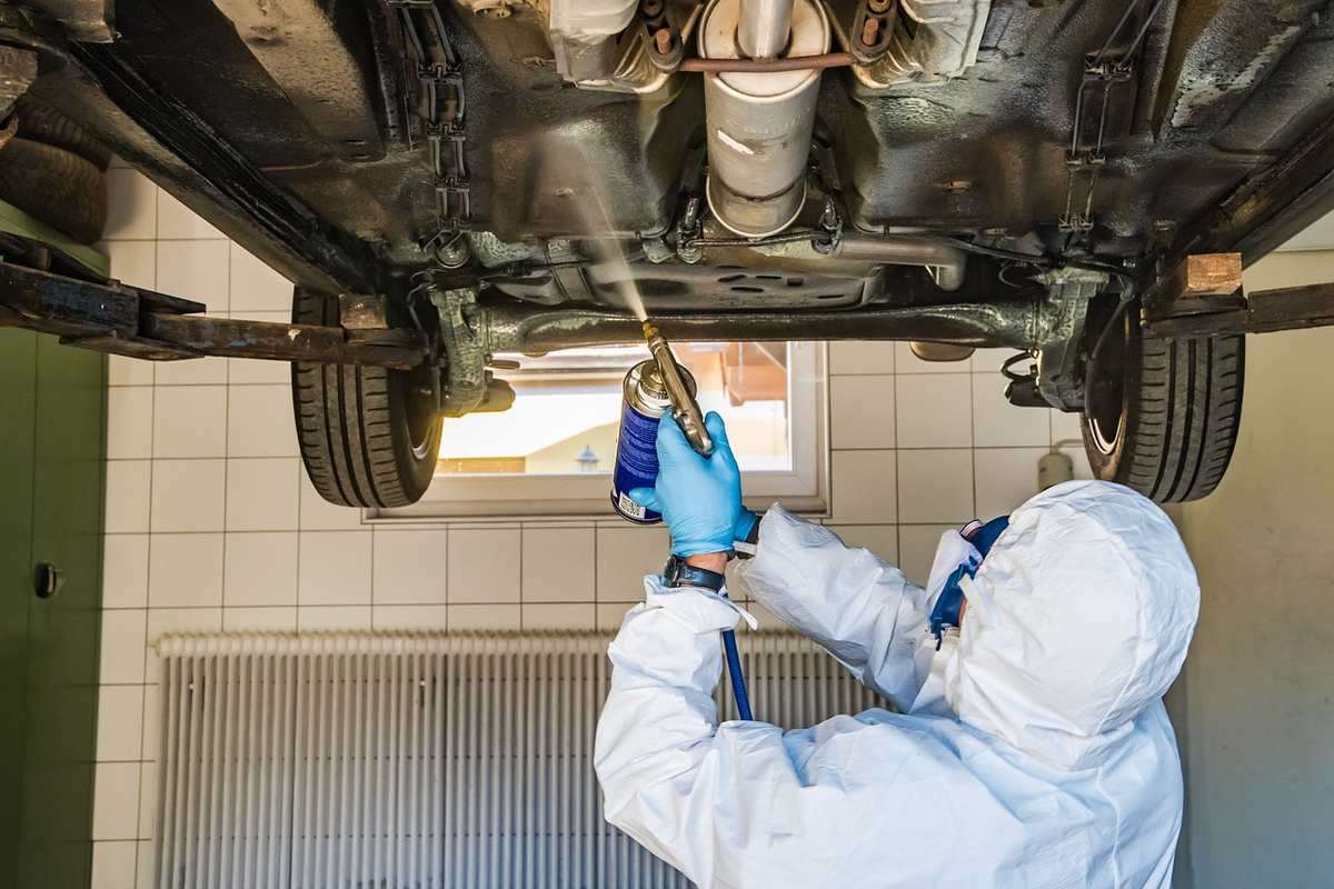 Technicien nettoie sous un véhicule soulevé dans un garage