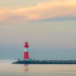 Un phare rouge et blanc sur une jetée, deux silhouettes, mer calme, ciel crépusculaire