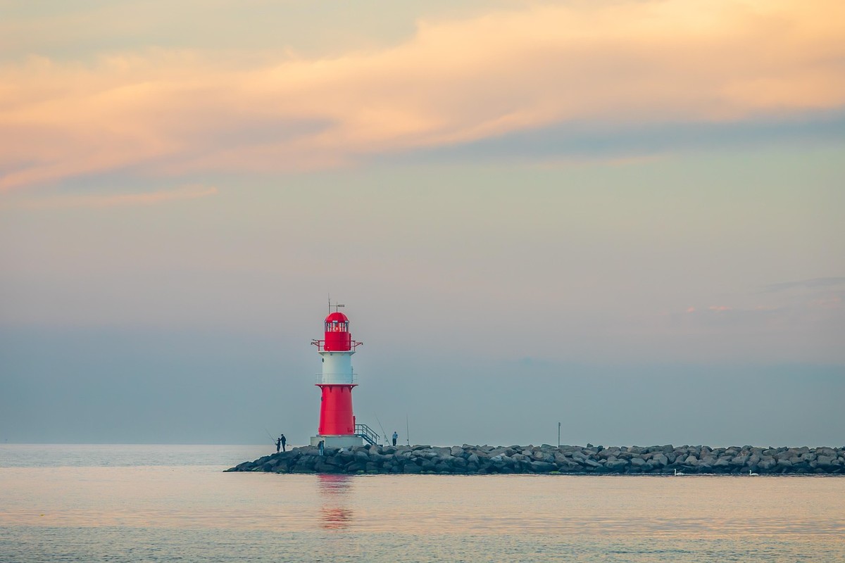 Un phare rouge et blanc sur une jetée, deux silhouettes, mer calme, ciel crépusculaire