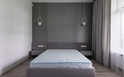 Un lit avec matelas sur cadre gris, murs et rideaux dans chambre
