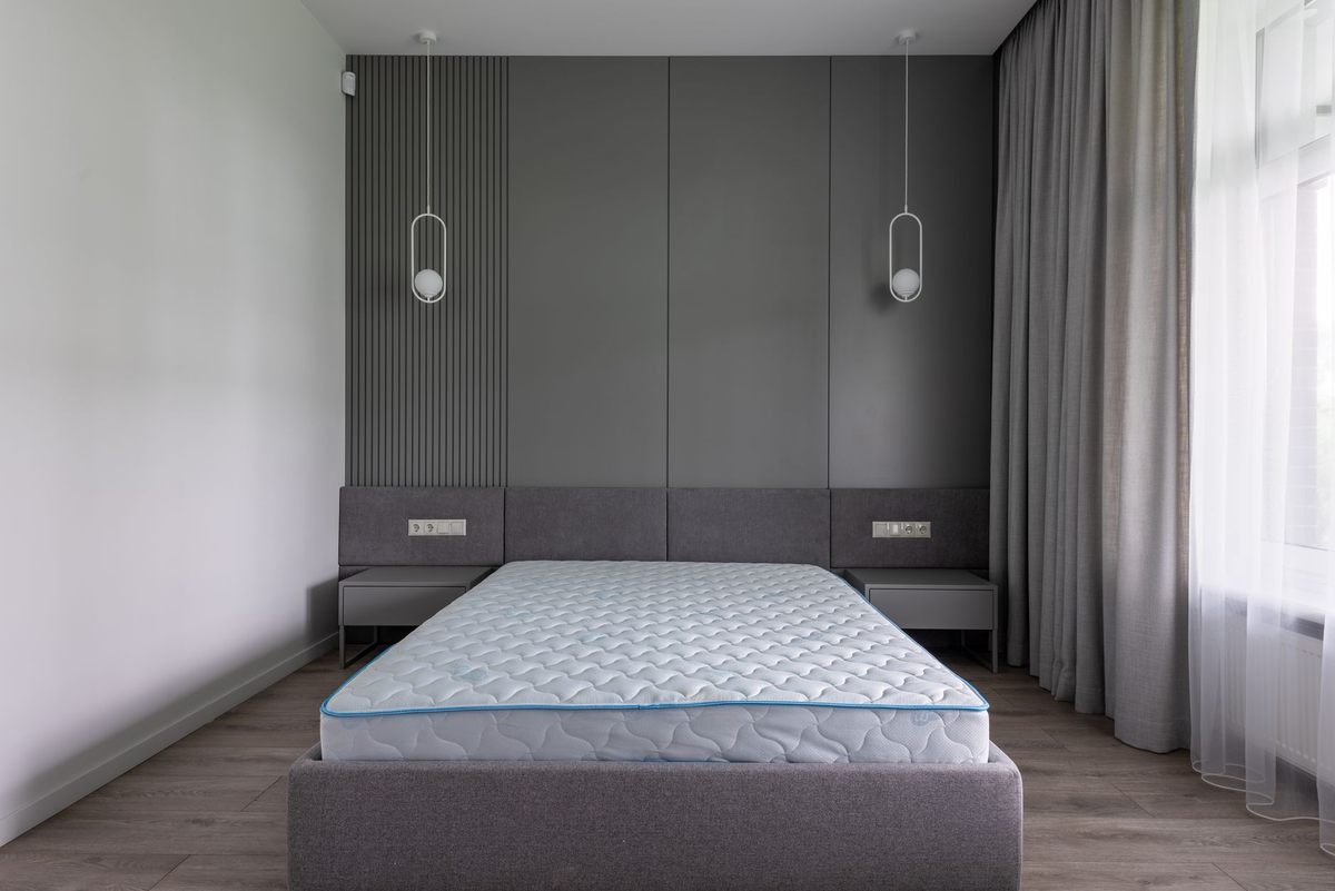Un lit avec matelas sur cadre gris, murs et rideaux dans chambre