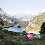 Tente rose et turquoise plantée en montagne près d'un lac entouré de pics rocheux