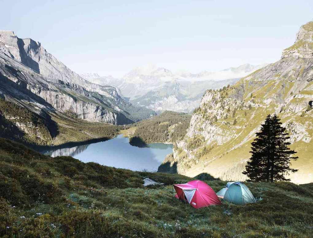 Tente rose et turquoise plantée en montagne près d'un lac entouré de pics rocheux