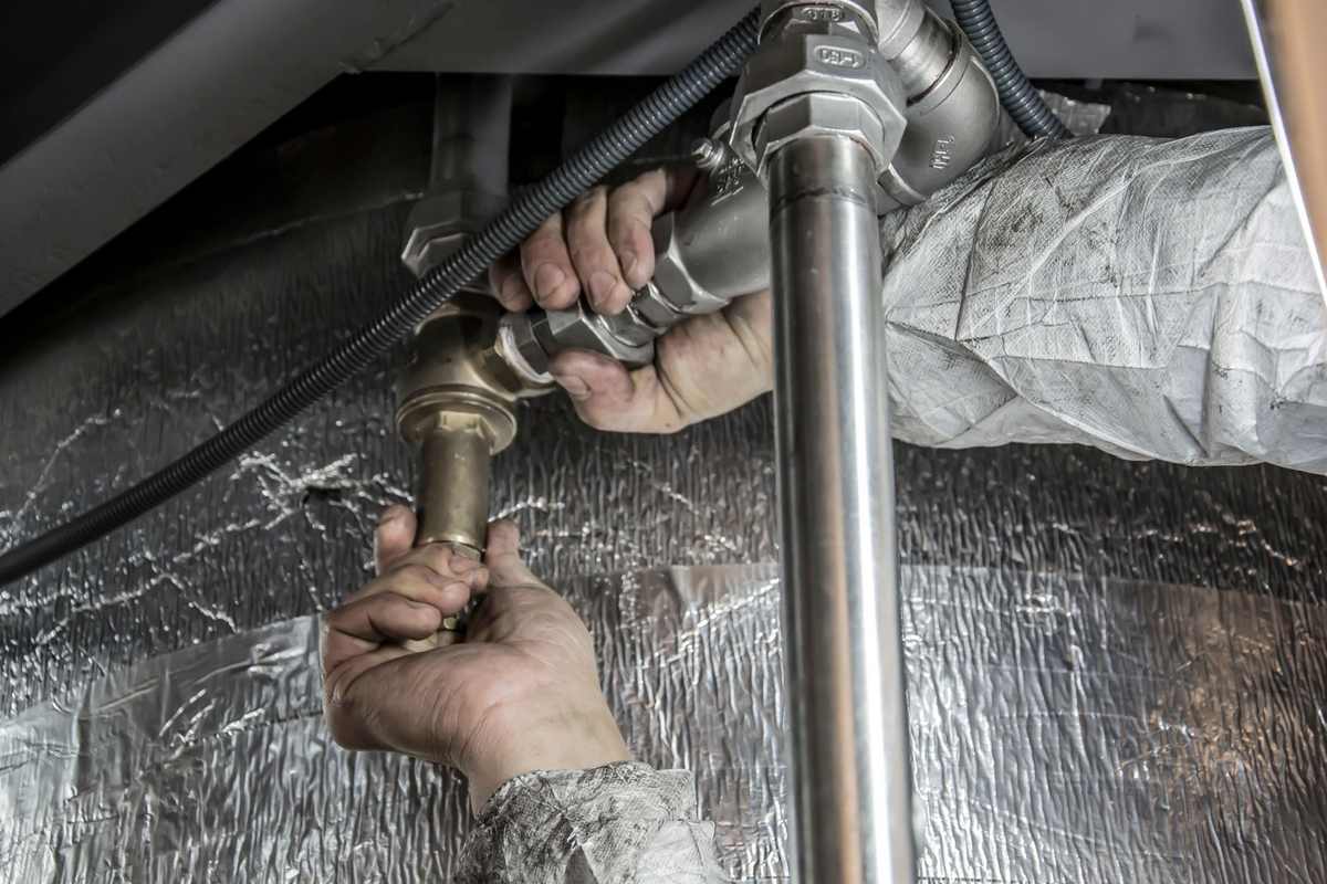 Mains gantées manipulant des tuyaux métalliques sous un véhicule Mains gantées manipulant des tuyaux métalliques sous un véhicule